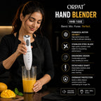 A woman in a black outfit blends orange juice in a clear glass using an ORPAT HHB-100E hand blender. The background is black with product feature callouts and icons on the right side.