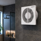 A white Bajaj wall-mounted exhaust fan installed on a dark gray tiled bathroom wall, with a shower area visible in the background.