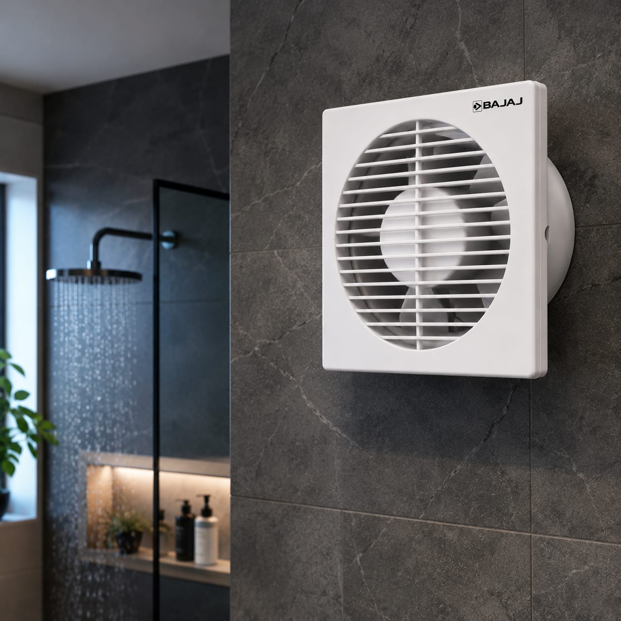 A white Bajaj wall-mounted exhaust fan installed on a dark gray tiled bathroom wall, with a shower area visible in the background.